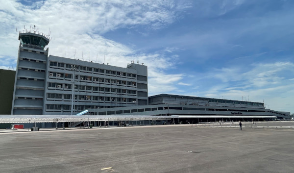 Airport view of building with air traffic control tower and terminal under a cloudy sky.